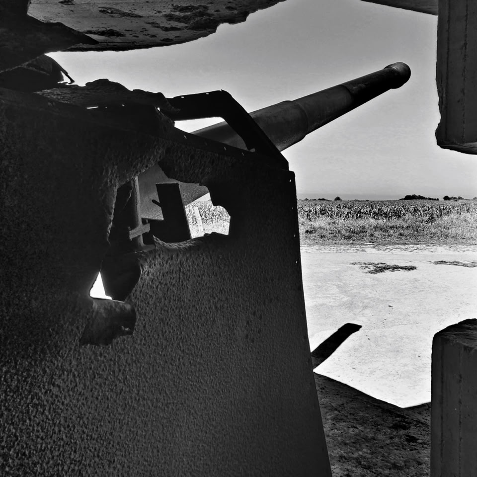 A black and white image of a large caon mounted on a vehicle, with a view of a barren landscape in the background. Normandie, France