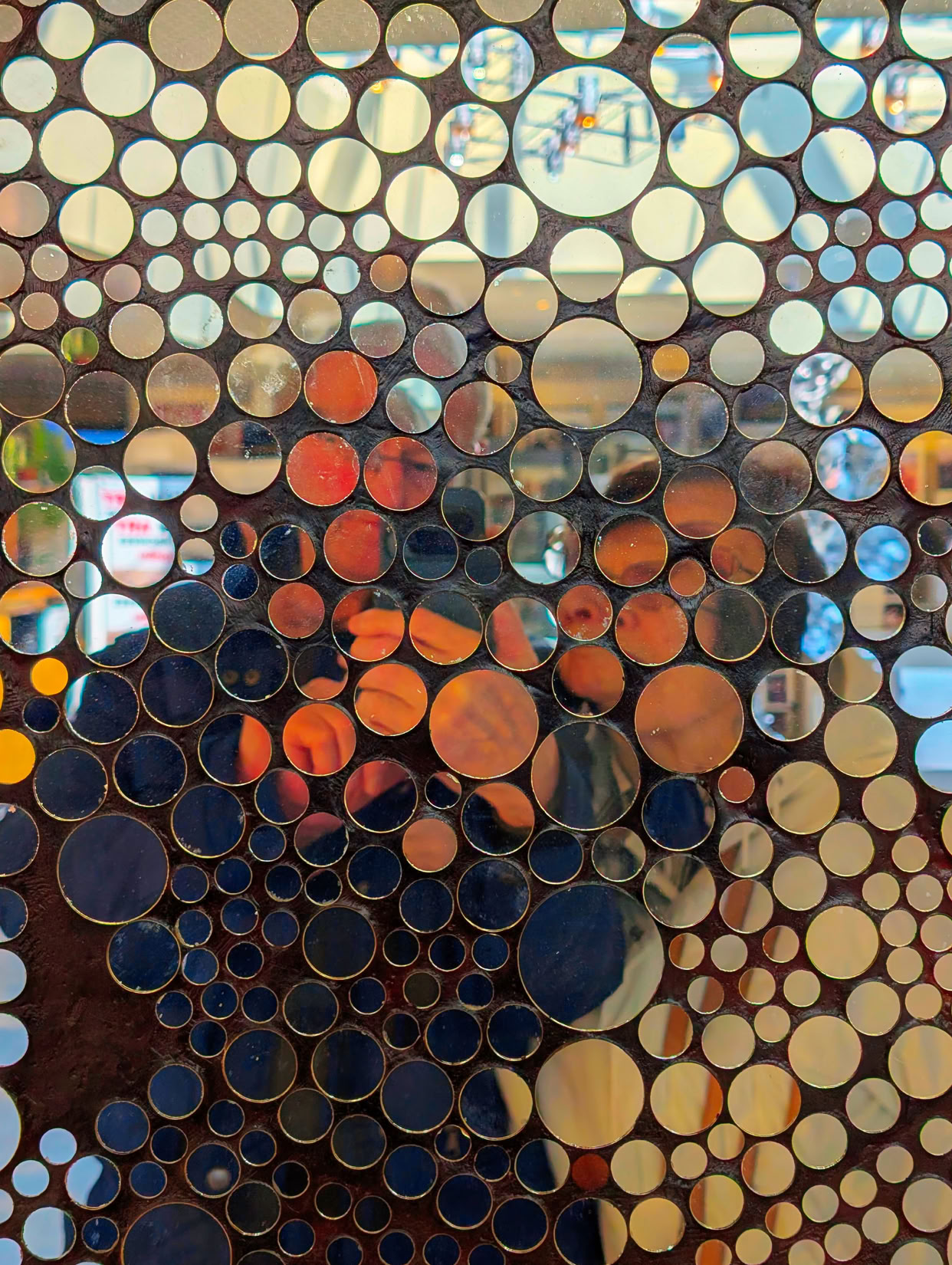 A mosaic of circular mirrors reflecting various colors and shapes of people