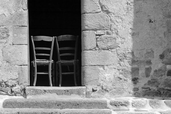 Two wooden chairs placed side by side in a doorway of a stone building. Church.