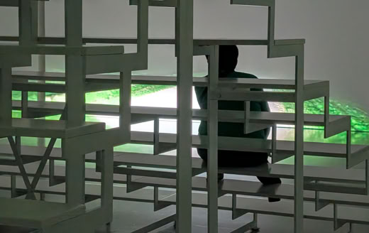 A person sitting on a geometric metal structure with a glowing green light in the background.