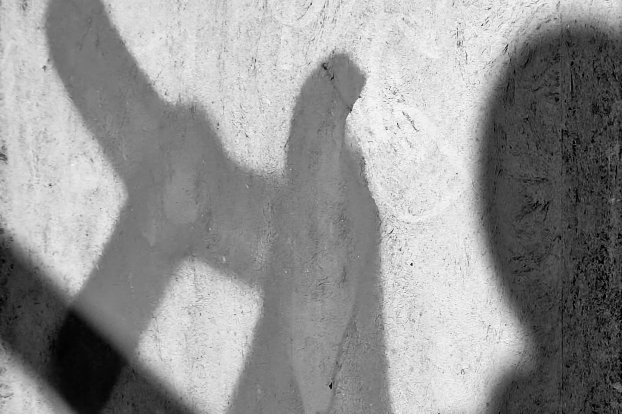 Shadow of a person holding a hammer against a textured wall.