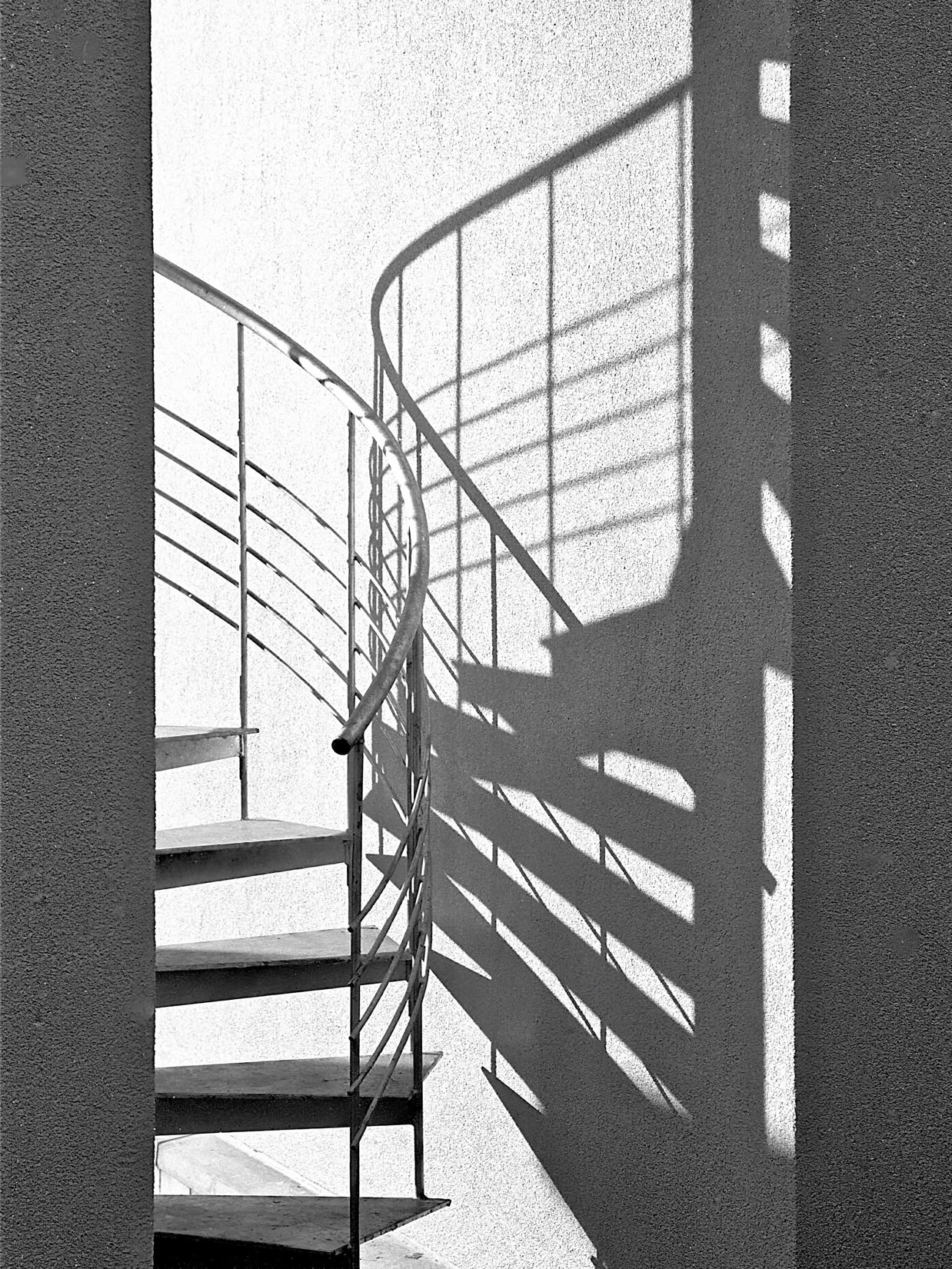 Spiral staircase with metal railings casting shadows on a wall.