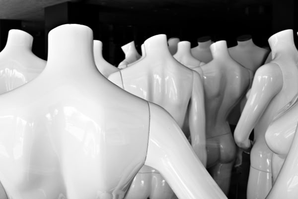 White, headless mannequins grouped closely together in a dimly lit space.