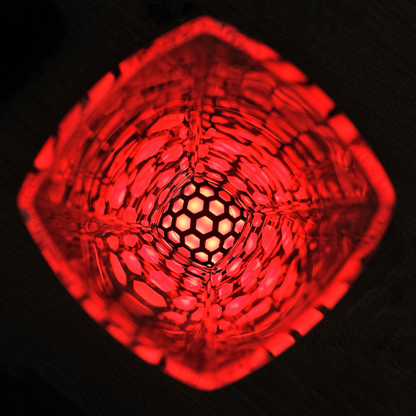 A red, intricately patterned, glowing object with a hexagonal grid at the center, viewed from above.