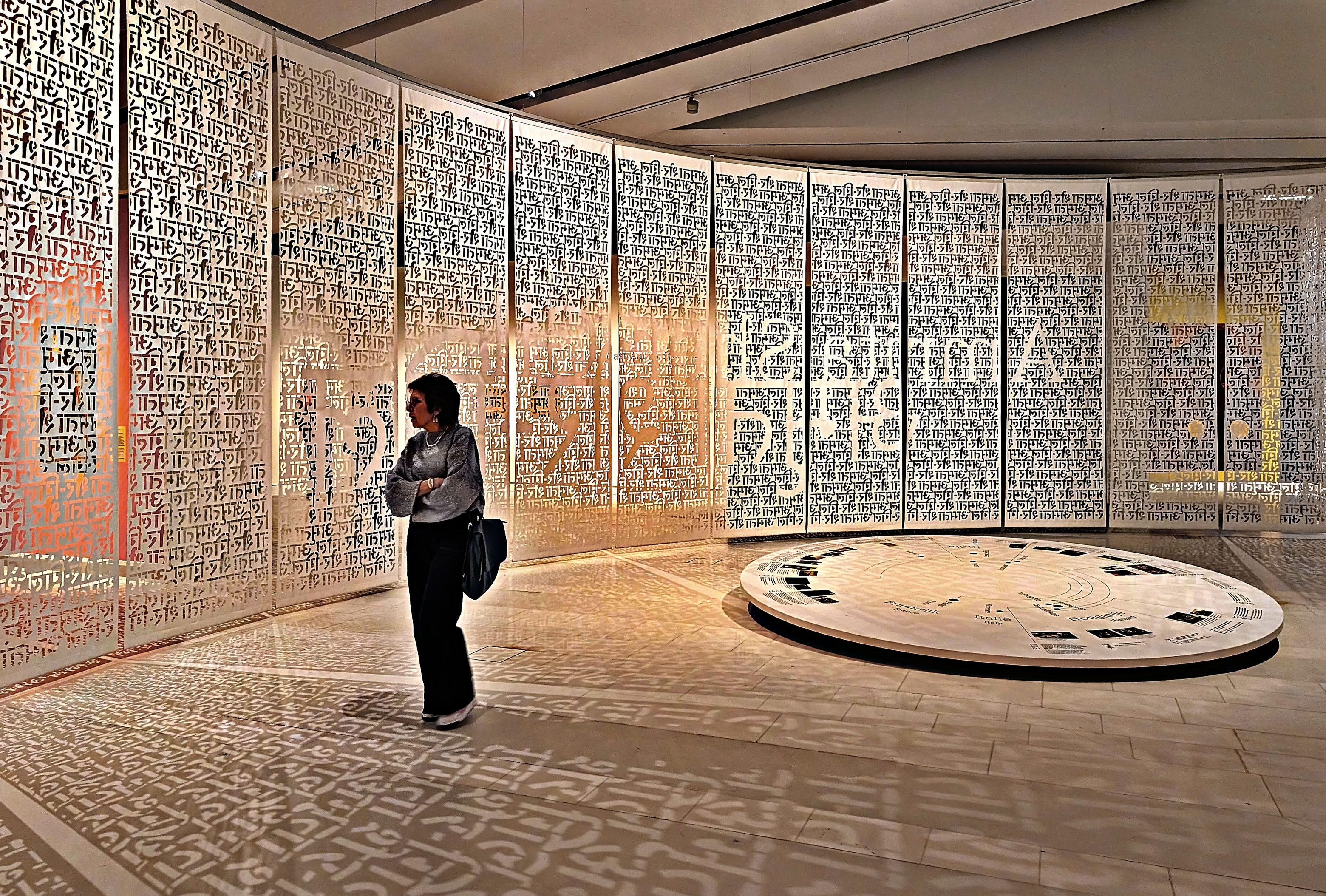 A person stands in the Drents Museum with walls covered in intricate patterns and symbols, and a circular display on the floor.