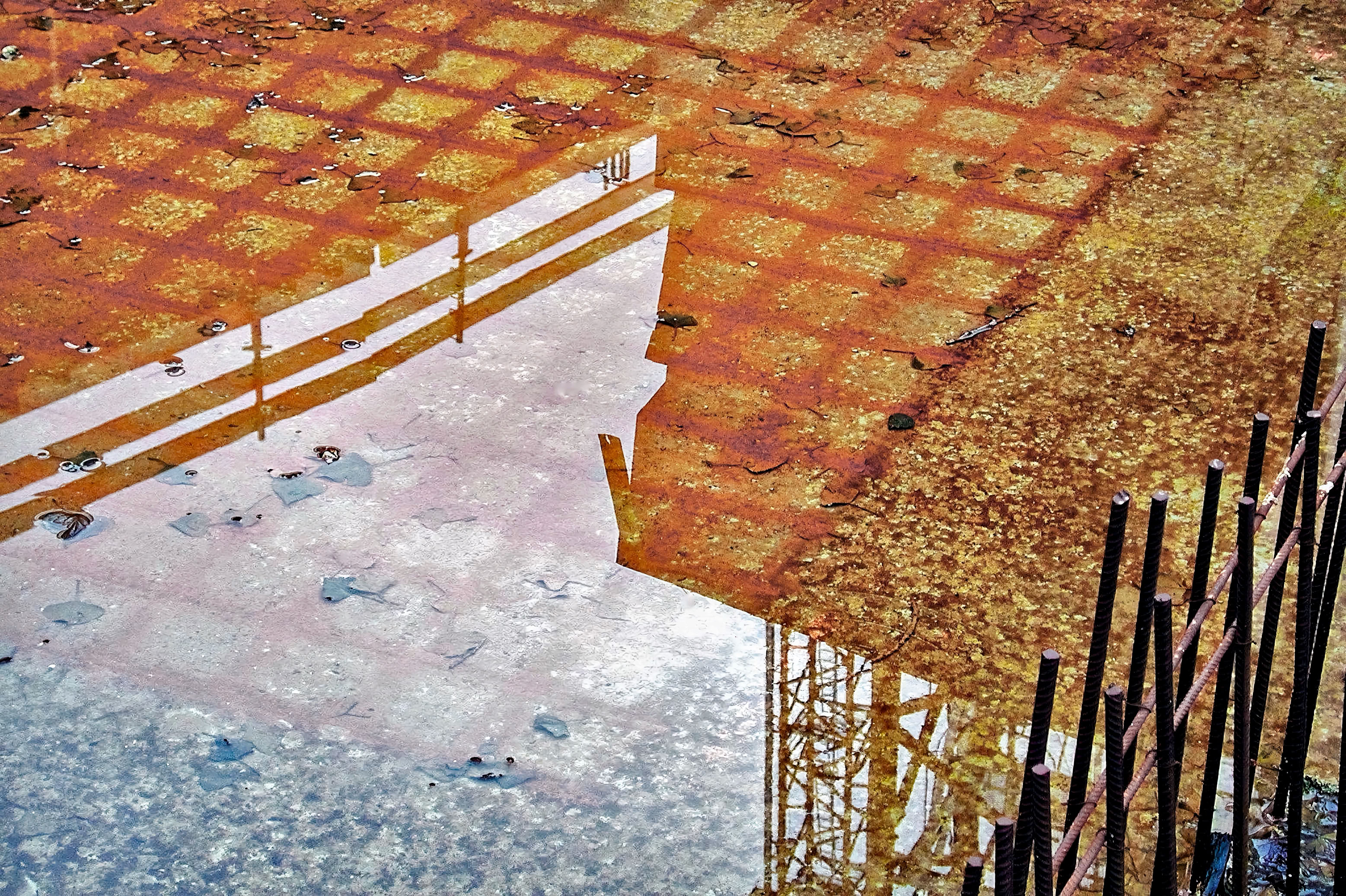 Rusty metal grid with water reflection and protruding metal rods.